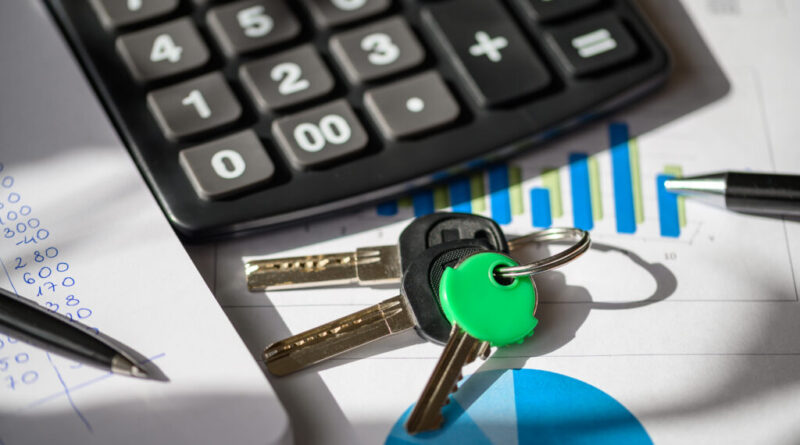 A calculator, a pen, and car keys on a desk with financial documents in the background.